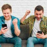 smiling-young-male-friends-looking-smart-phone-clenching-their-fist (1)