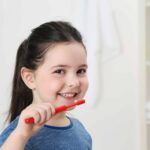 Smiling little girl brushing teeth, close up